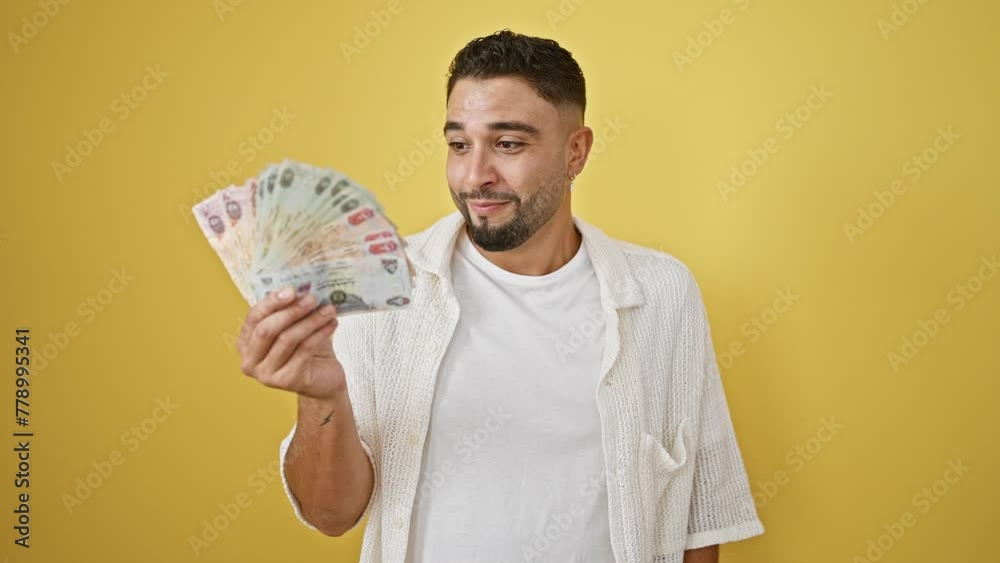 Ecstatic young arab man drenched in victory joy, hands raised high as he celebrates his win, smiling amid a torrent of united arab emirates banknotes. isolated against a sizzling yellow background. Ecstatic young arab man drenched in victory joy, hands raised high as he celebrates his win, smiling amid a torrent of united arab emirates banknotes. isolated against a sizzling yellow background.