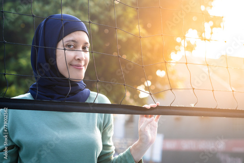 Muslim woman in hijab with brown eyes holding volleyball net in morning sunlight. photo