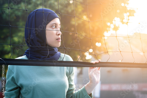 Muslim woman in hijab with brown eyes holding volleyball net in morning sunlight. photo