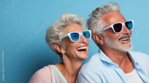 An elderly couple wearing blue sunglasses is smiling.