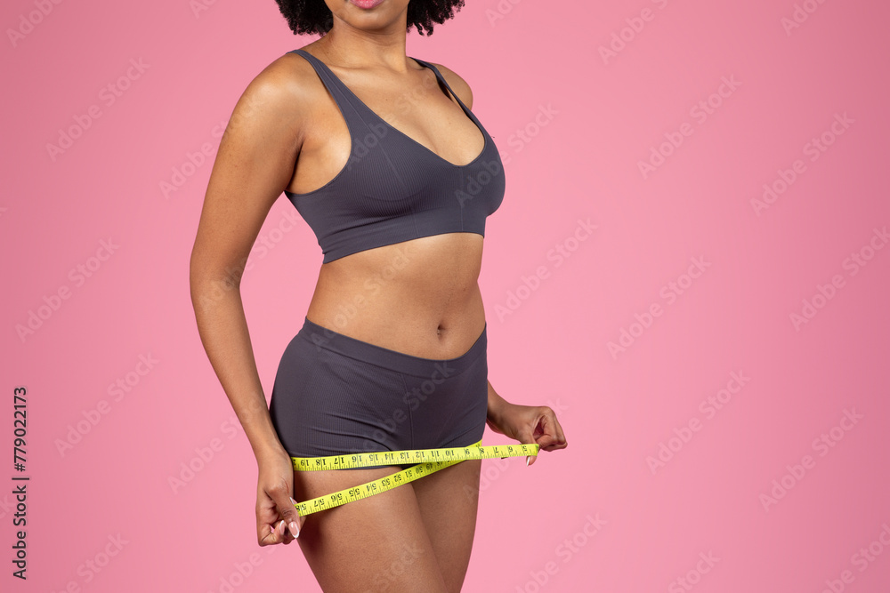 Woman measuring waist with a bright yellow tape measure - obrazy, fototapety, plakaty 
