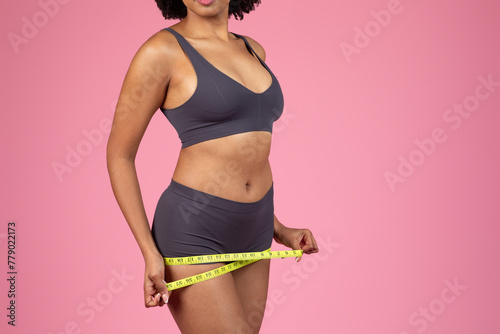 Woman measuring waist with a bright yellow tape measure © Prostock-studio