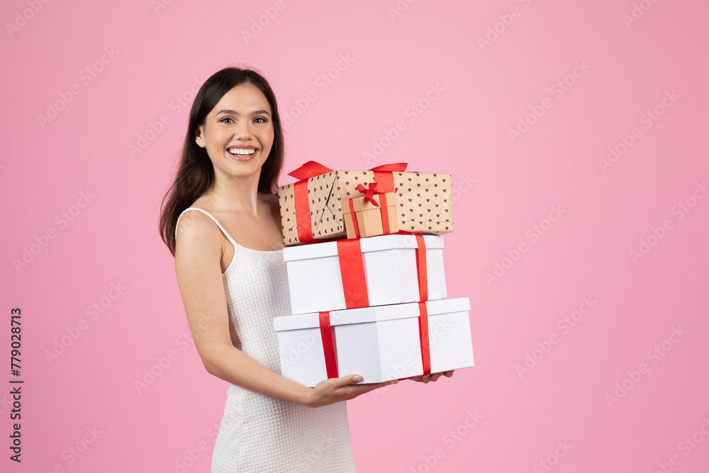 Woman smiling holding stack of gifts on pink background Woman smiling holding stack of gifts on pink background