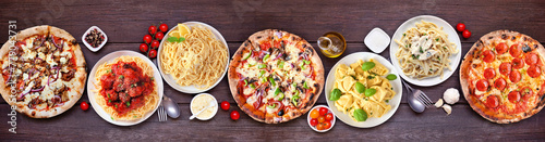 Delicious Italian food table scene. Variety of pizzas and pastas. Above view on a dark wood banner background.