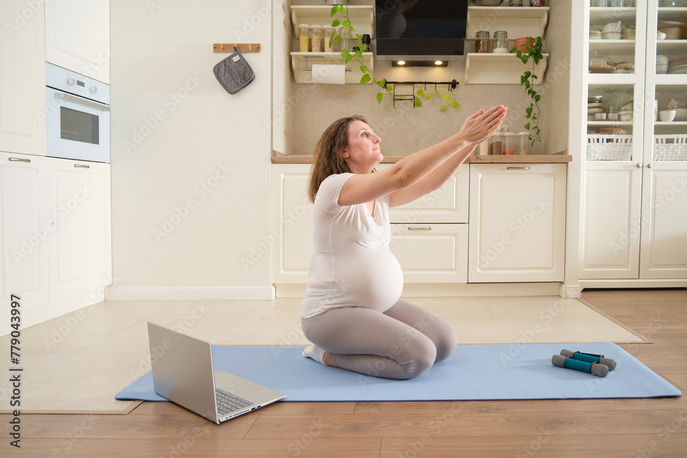 Pregnant woman doing sports in the home kitchen and doing hand stretching Pregnant woman doing sports in the home kitchen and doing hand stretching