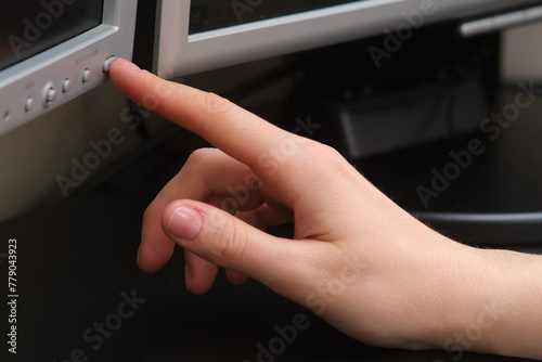 A woman s hand presses the power button on a computer monitor