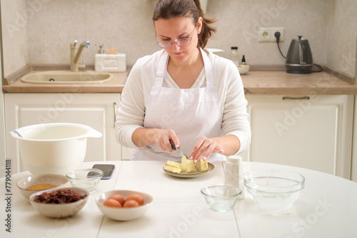 Woman in white apron cutting butter on plate with knife in the kitchen at home. Process of cooking pecan pie in home kitchen for American Thanksgiving Day.