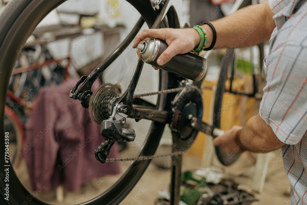 Close up of repairman is holding spray lubricant in his hand to lubricate the bike chain Close up of repairman is holding spray lubricant in his hand to lubricate the bike chain