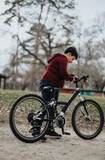 Active young adult examining his mountain bike before riding in an outdoor park setting with trees in the background.