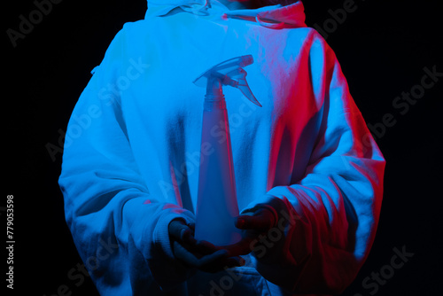Person in hoodie with spray bottle, under red and blue light effects