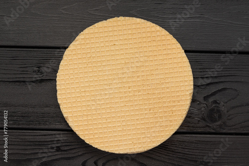 Round waffle on a dark wooden surface, centered, top view.