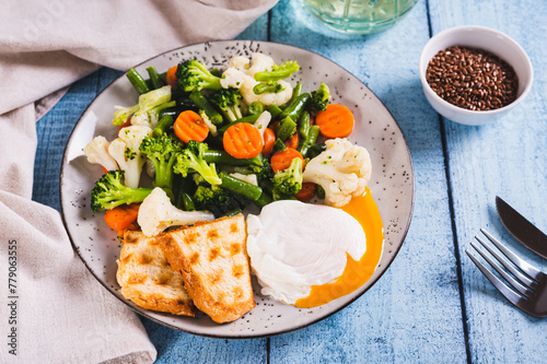 Poached egg, broccoli, cauliflower, green beans and carrots on a plate on the table