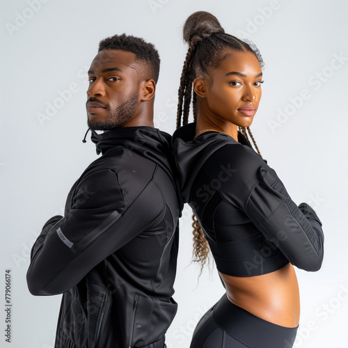 A man and woman stand back to back wearing black athletic wear.