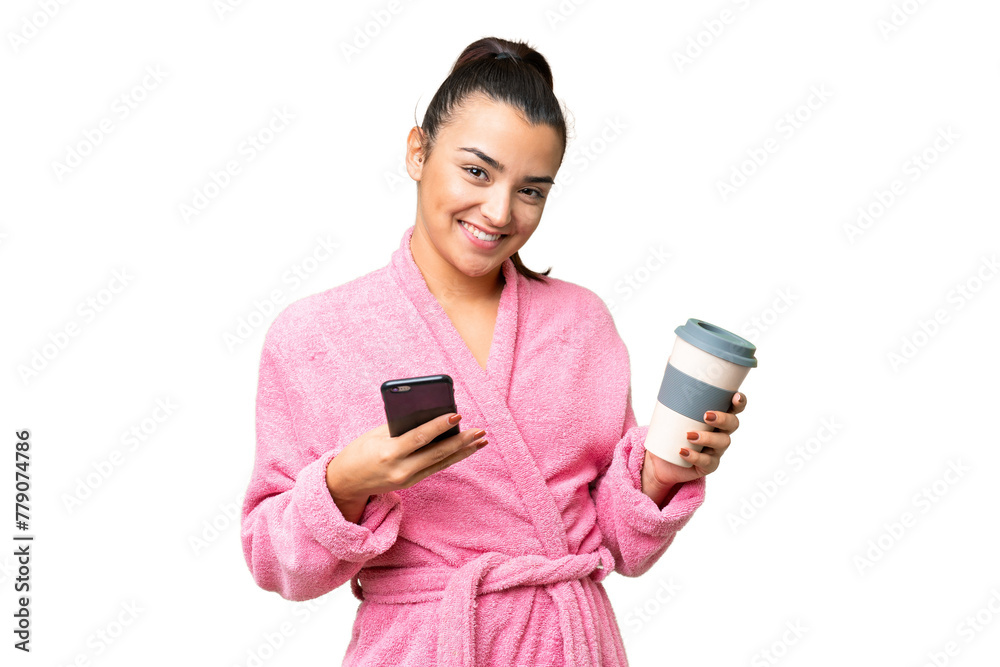Young woman in a bathrobe over isolated chroma key background holding coffee to take away and a mobile Young woman in a bathrobe over isolated chroma key background holding coffee to take away and a mobile