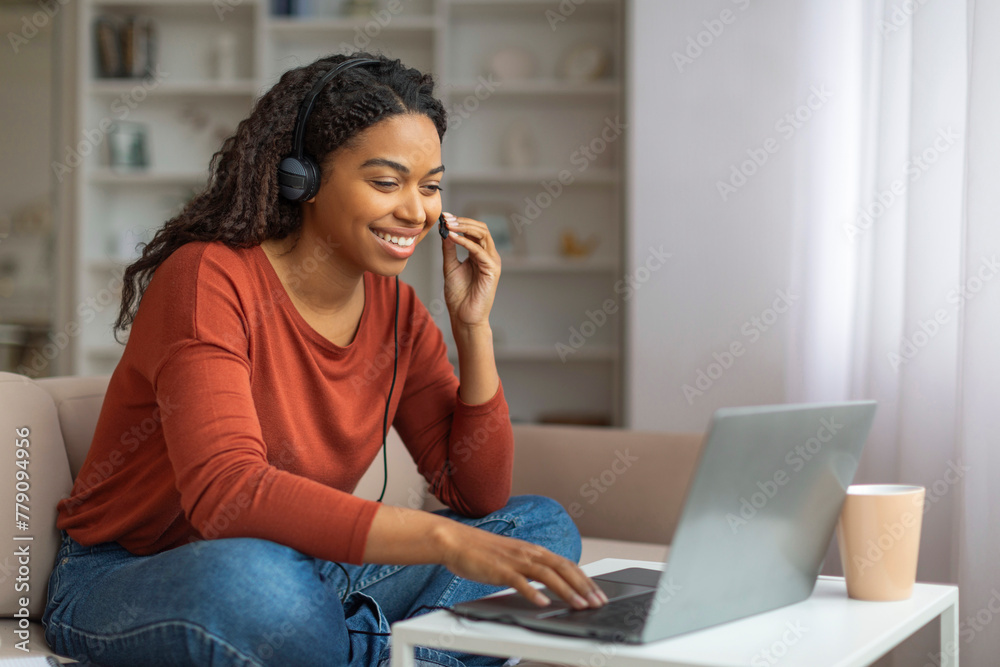Fototapeta premium Smiling Black Woman Using Laptop and Headset for Video Call at Home