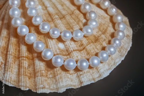 beautiful women's necklace made of white natural pearls with a clam shell on a black matte background