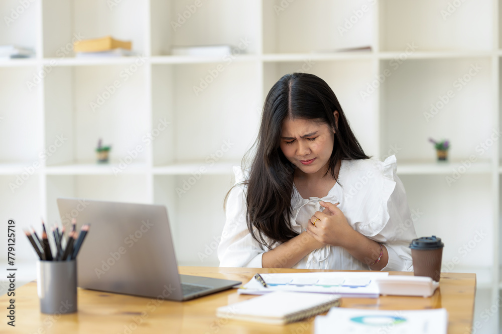 A concerned businesswoman at her office desk feeling discomfort, clutching her chest with a pained expression, workplace health issues.