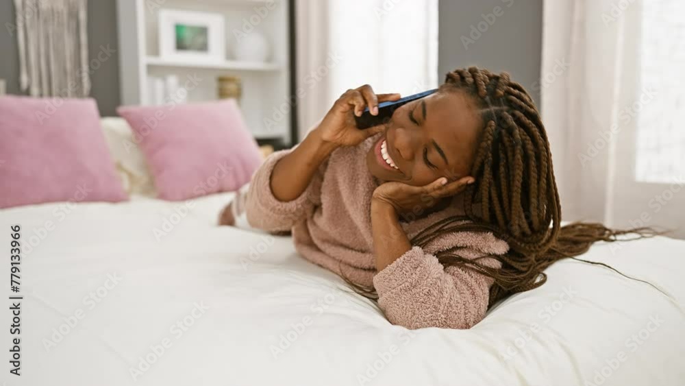 A cheerful woman with braids talking on a phone while lying in a cozy bedroom setting, exuding a sense of comfort and joy. A cheerful woman with braids talking on a phone while lying in a cozy bedroom setting, exuding a sense of comfort and joy.