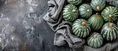   A table holds a stack of watermelons, accompanied by a cloth and a bag