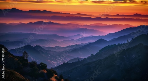 a sunset over a mountain range with a bright orange sun in the distance and a hazy sky above it