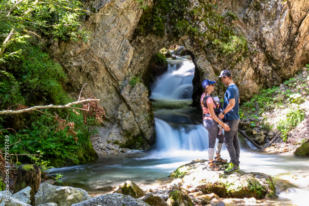 Family standing on rock with scenic view of majestic waterfall cascade of Bodentaler Felsentor, Tscheppaschlucht, Loibl Valley, Karawanks, Carinthia, Austria. Water cascading down cliff face into pool Family standing on rock with scenic view of majestic waterfall cascade of Bodentaler Felsentor, Tscheppaschlucht, Loibl Valley, Karawanks, Carinthia, Austria. Water cascading down cliff face into pool