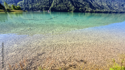 Panoramic view of alpine landscape seen from east bank of lake Weissensee in Carinthia, Austria. Tranquil forest in serene landscape amidst remote untouched nature in summer. Pristine turquoise water photo