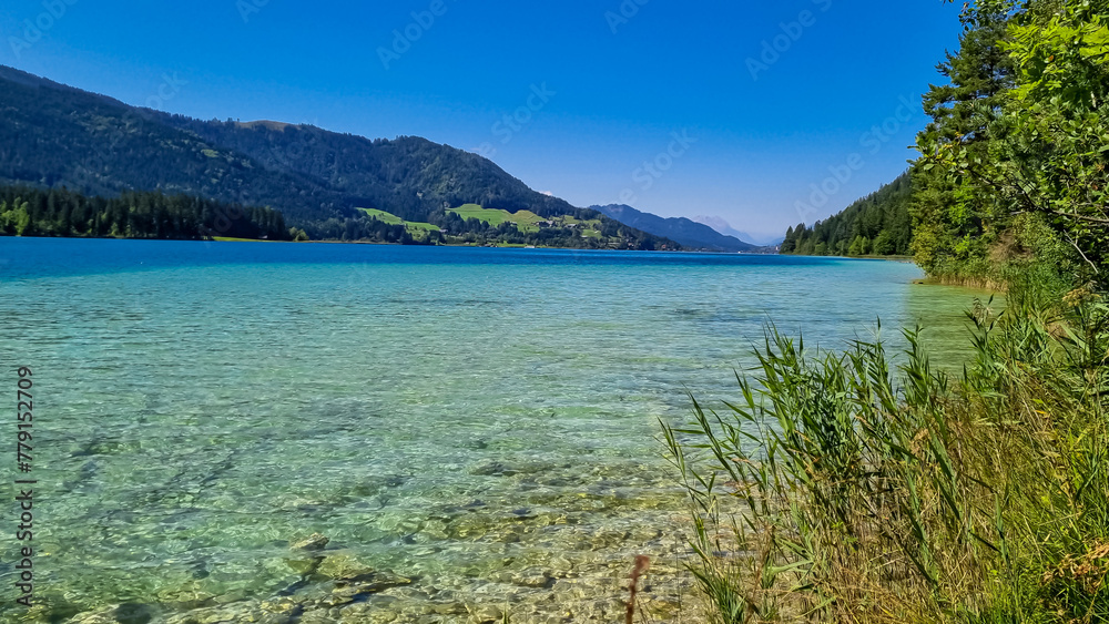 Panoramic view of alpine landscape seen from east bank of lake Weissensee in Carinthia, Austria. Tranquil forest in serene landscape amidst remote untouched nature in summer. Pristine turquoise water