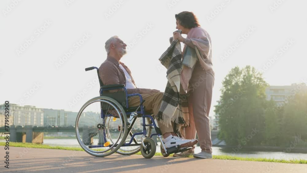 Old man in wheelchair walking with caregiver senior woman in park. Elderly family couple woman supporting taking care of paralyzed man in chair for people with disability outdoor. Rehabilitation Old man in wheelchair walking with caregiver senior woman in park. Elderly family couple woman supporting taking care of paralyzed man in chair for people with disability outdoor. Rehabilitation