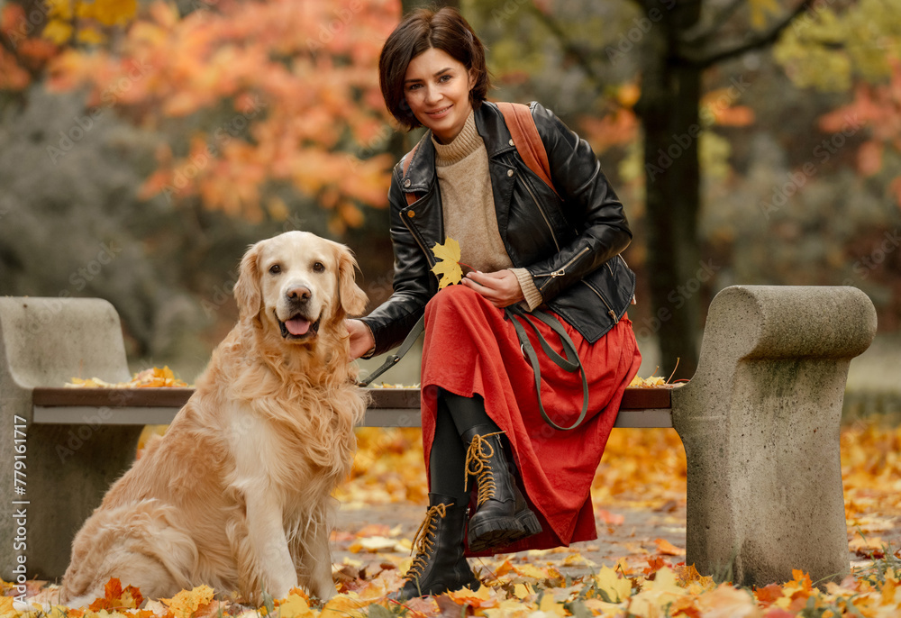 A young woman sitting on a bench in an autumn park and petting a Golden Retriever dog