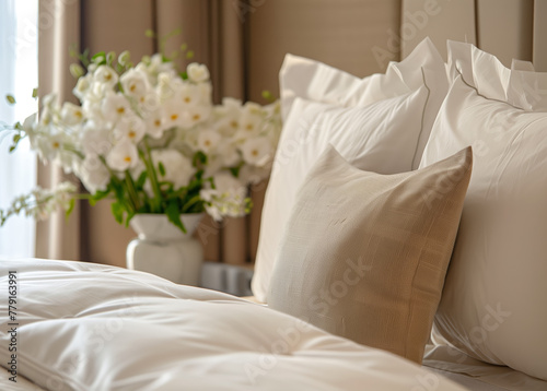Luxurious Bedding Close-up with Fresh Flowers. Close-up of crisp white bed linen and textured beige pillows with a bouquet of white flowers in soft focus