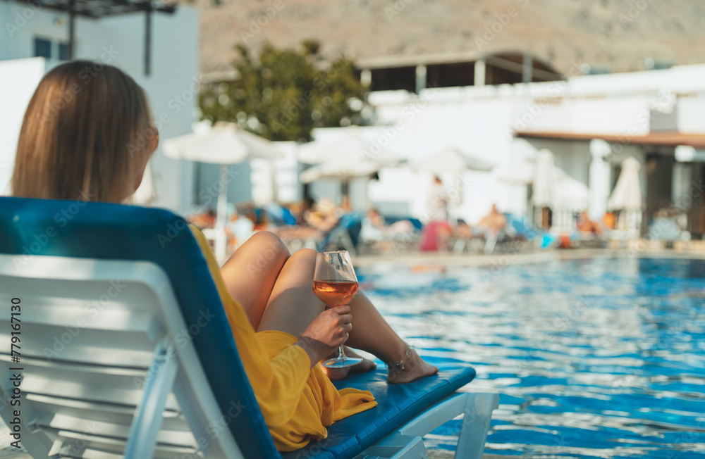 Woman with wine relaxing by the swimming pool.