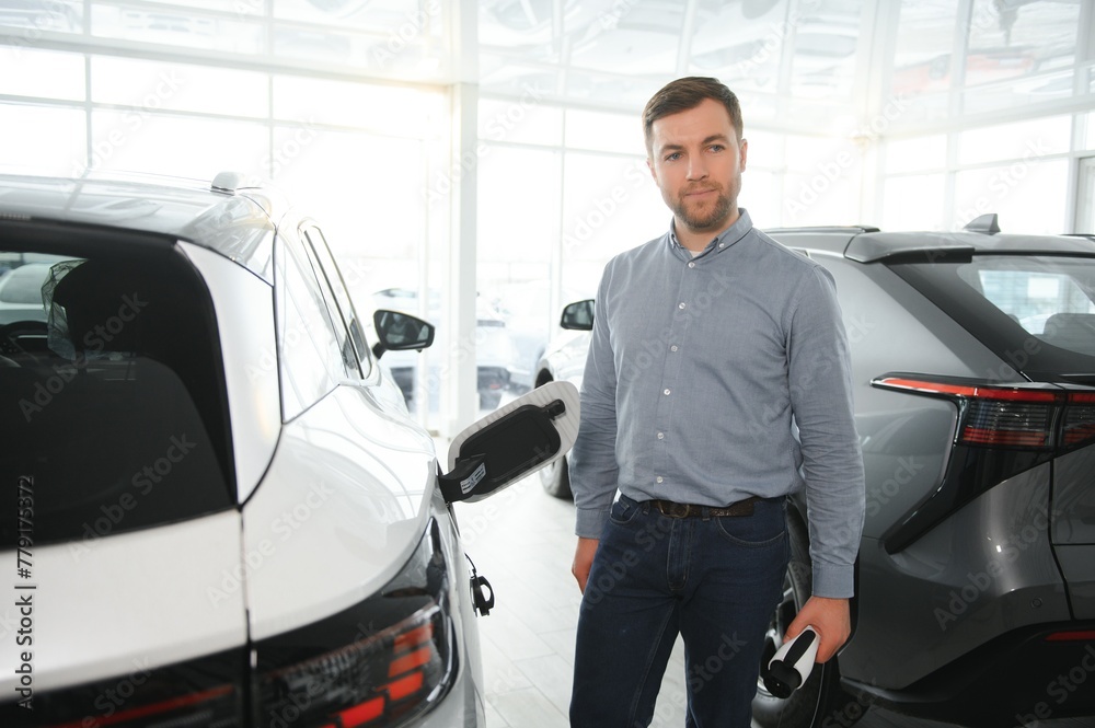 Concept of buying electric vehicle. Handsome business man stands near electric car at dealership Concept of buying electric vehicle. Handsome business man stands near electric car at dealership