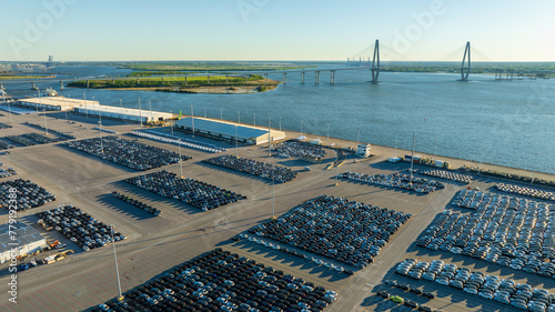 New cars parked in orderly rows at a port parking lot with the expansive Arthur Ravenel Jr. Bridge in the background in Charleston, SC. photo