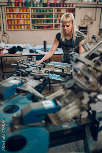 Graphic worker manipulating screen printing press at printing shop.