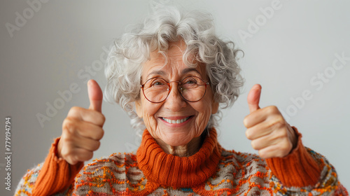 Femme joyeuse levant les pouces en l'air, photographie sur fond blanc, grand-mère de 70 ans avec des lunettes et un col roulé photo
