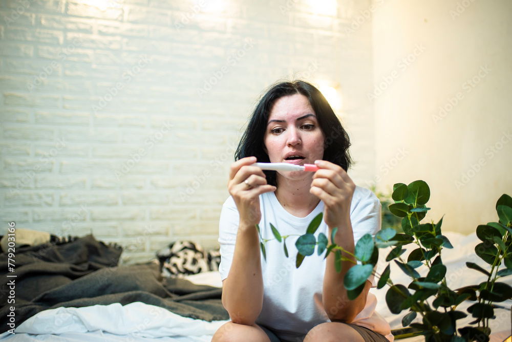 surprised 41 year old woman looking at pregnancy test while sitting on bed in room surprised 41 year old woman looking at pregnancy test while sitting on bed in room