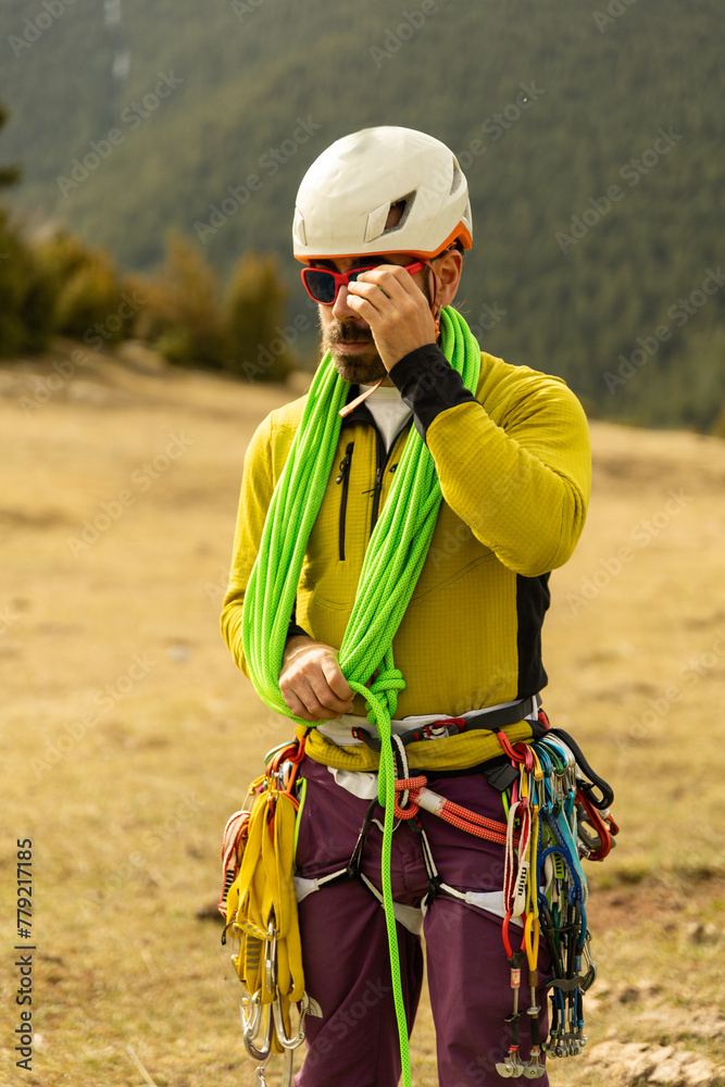 A man in a yellow shirt is wearing a green rope around his neck. He is wiping his nose with his hand