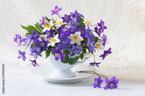 Bouquet of spring flowers hepatica and anemones in a cup on a white wooden table, beautiful card