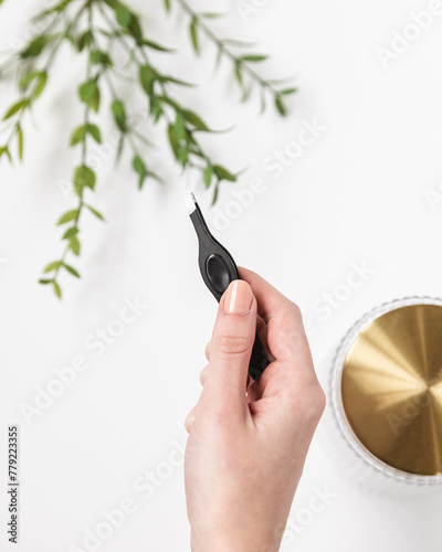 Woman holding pair of black tweezers over trendy and modern bathroom counter
