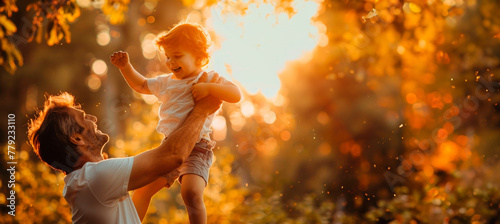 A young male father lifts a small, smiling, joyful child into the air with one arm outstretched in the sunlight in the park. Attitude of children and parents. Father's Day. Banner. Copy space