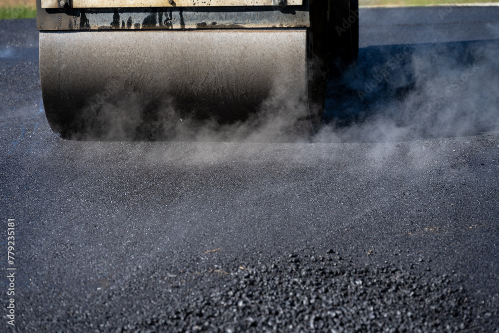 Closeup of a steamroller on freshly paved driveway to compact the hot asphalt, road construction project
