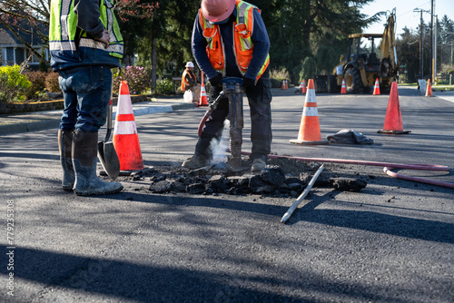 Fotografie Construction workers using a jackhammer to dig up freshly laid asphalt to find t
