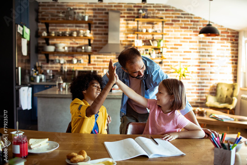 Father helping children with homework at kitchen table photo