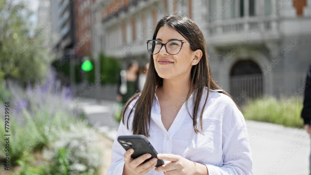 Young beautiful hispanic woman smiling happy using smartphone in the streets of Madrid Young beautiful hispanic woman smiling happy using smartphone in the streets of Madrid