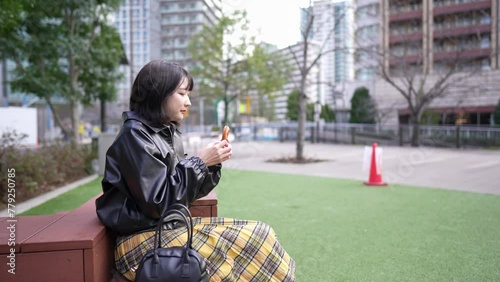 Slow motion video of a young Japanese woman in her 20s eating churros in a park around Gotanda Station, Shinagawa-ku, Tokyo in winter 冬の東京都品川区五反田の駅周辺の公園でチュロスを食べる若い２０代の日本人女性のスローモーション映像 photo