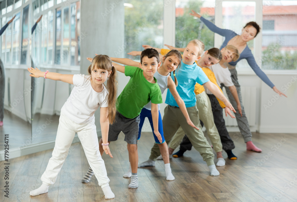 Group of focused tween children standing akimbo in row one by one, learning movements of folk dance in choreography lesson