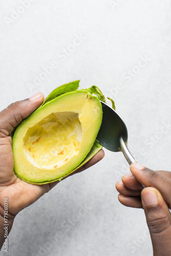 Overhead view of green avocado being peeled using a spoon, top view of avocado being de-skinned with a silver spoon