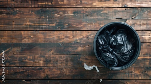 Trash can with a black plastic bag inside, on a wooden background, viewed from above. photo
