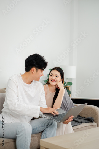 Young couple shares a joyful moment while looking at a laptop together on a cozy couch in a bright living room.