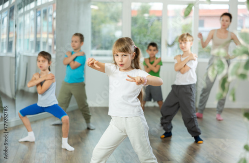 Dynamic little girl training break-dance poses in dancehall with trainer and other attendees of dancing courses